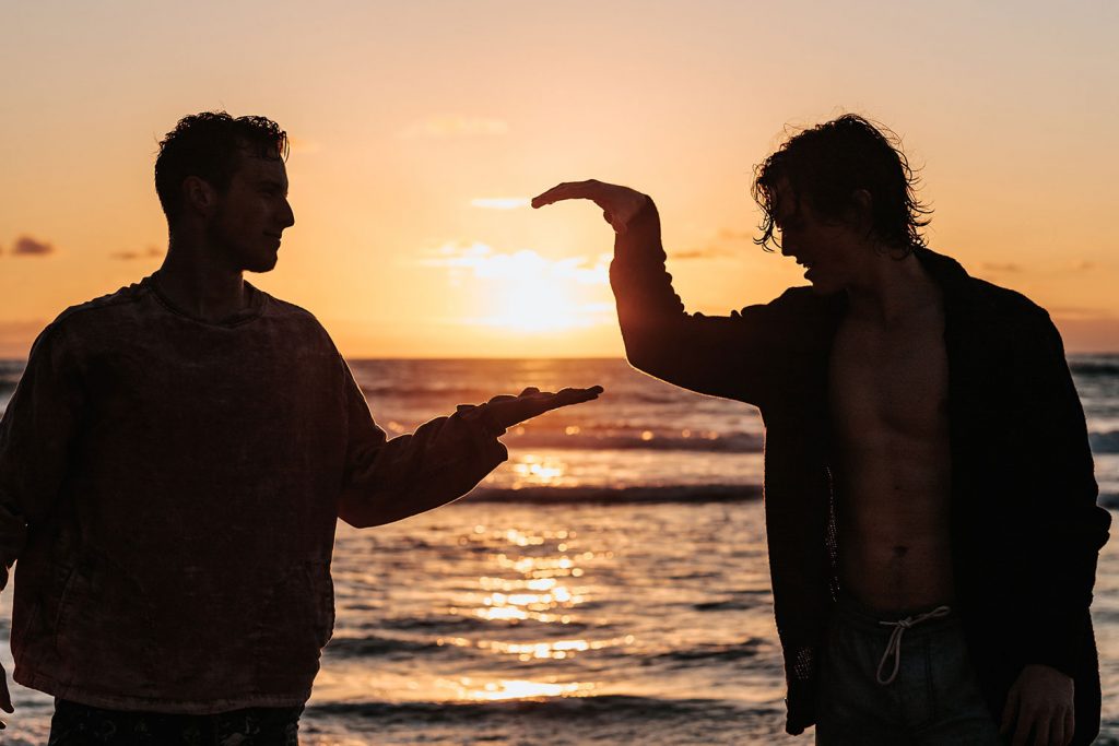 Two men on a beach giving each other high fives with a sunset behind it