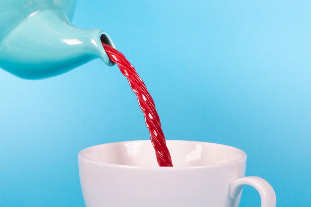 A blue teapot pours a Twizzler into a white tea cup with a bright blue background